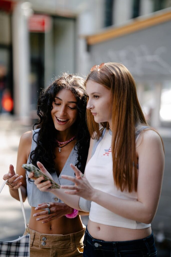 Friends sharing a joyful moment while looking at a smartphone on a sunny city street.